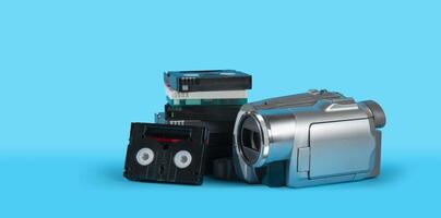 old camera next to a black mini DV cassette tower on a blue surface against blue background photo
