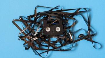 Old black mini DV cassette with tangled tape surrounding the cassette photo