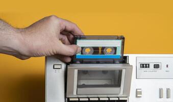 man's hand inserting old music cassette into aluminum recorder against yellow background photo