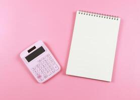 flat lay of pink calculator with blank page opened notebook on pink background. business and education concept. photo