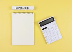 flat layout of opened blank page notebook with wooden calendar September and white calculator on yellow background. monthly financial plan concept. photo