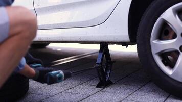 Young man in unscrewing lug nuts on car wheel in process of new tire replacement,using wrench while changing flat tire on the road. video