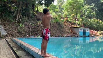 back view of asian man standing in the poolside stretching his arms and legs before swimming in the natural pool video