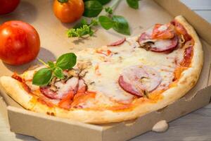 cooked pizza with salami and sausage in a box on a wooden table photo