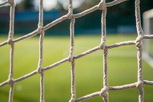 Closeup white soccer net, intricate knots, blurred well maintained field, sunlight photo
