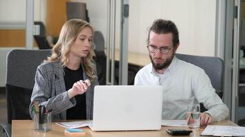 A woman in a plaid blazer pointing at a screen while a bearded man in glasses looks on intently. Professionals working together about market data reports in office. video
