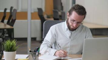 An office man concentrate working on his desk. Businessman looking at the screen and writing in notebook. Planning. video
