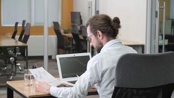 A side view of a man analyzing and calculating the complex market charts on his computer screen and the handheld data report, stretching his arms for having a good result. video