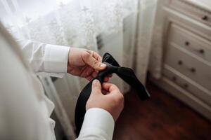 A man is getting ready for a formal event and is adjusting his tie. Concept of preparation and attention to detail, as the man carefully ties his tie to ensure it looks neat and professional photo