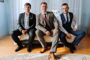 Three men in suits are sitting on a couch. They are all wearing ties and are posing for a picture. Scene is formal and professional photo