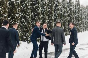 A group of men are standing in the snow, dressed in suits and ties. They are laughing and hugging each other, enjoying the winter weather photo