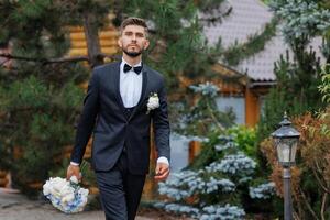 A man in a suit and tie is walking down a path with a bouquet of flowers in his hand photo