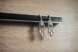 A pair of earrings with a diamond design are sitting on a wooden surface. The earrings are large and shiny, and they appear to be a statement piece. The wooden surface adds a rustic photo