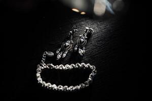 A pair of earrings and a bracelet are displayed on a dark table. The earrings are large and shiny, while the bracelet is smaller and more delicate. Scene is elegant and sophisticated photo