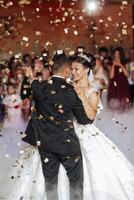 A bride and groom are dancing in the air with confetti falling around them. Scene is joyful and celebratory, as the couple is enjoying their wedding reception photo