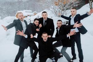 A group of men in suits are posing for a picture in the snow. Scene is lighthearted and fun, as the men are all smiling and enjoying the moment photo