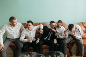 A group of men are sitting on a couch, laughing and hugging each other. Scene is happy and friendly photo