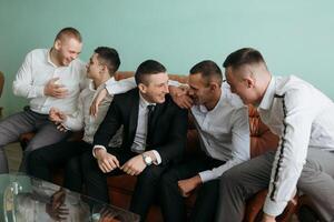 A group of men are sitting on a couch, laughing and hugging each other. Scene is happy and friendly photo