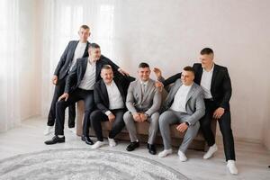 A group of men in suits are sitting on a couch. They are all smiling and seem to be enjoying each other's company photo