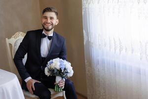 A man in a suit and tie is sitting in a chair with a bouquet of flowers in his lap. He is smiling and he is happy photo