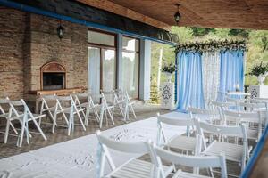 A wedding reception is taking place in a beautiful outdoor setting. The chairs are arranged in rows, and the tables are set up with vases and flowers. The chairs are all white photo