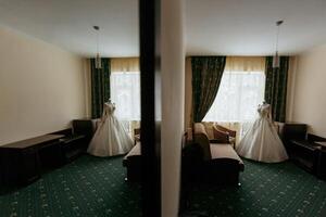 A bride's dress is displayed in a room with a green carpet. The room has a mirror on the wall and a couch photo