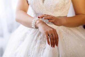 A woman in a white dress is wearing a pearl bracelet. She is standing in front of a window, and her hands are clasped together. Concept of elegance and sophistication photo
