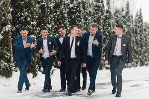 A group of men dressed in suits and ties are walking through the snow. They are all smiling and giving thumbs up to each other. Scene is cheerful and celebratory photo