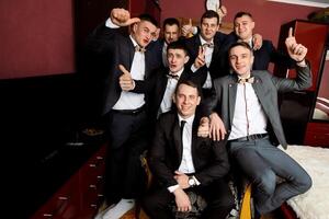 A group of men in suits are posing for a picture, with one man giving a thumbs up. Scene is celebratory and happy, as the men are dressed up and posing for a photo together