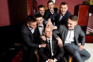 A group of men are posing for a picture, all wearing suits and ties. They are all smiling and seem to be enjoying each other's company. Scene is lighthearted and fun photo