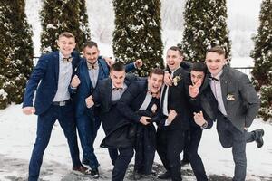 A group of men in suits posing for a picture in the snow. Scene is happy and celebratory, as they are all dressed up and posing for a photo together