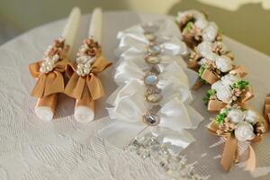 A table with candles and flowers. The candles are in different sizes and colors. The table is white and has a floral pattern photo