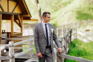 A man in a suit and tie stands on a wooden bridge. He is holding a white flower in his hand photo