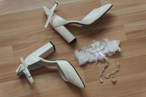 A pair of white shoes and a white garter are displayed on a wooden surface. Concept of elegance and sophistication, as the white shoes photo