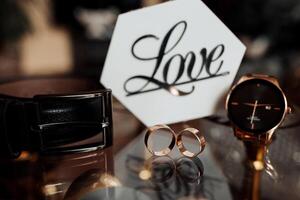 A watch, a ring and a belt are displayed on a table. The watch is a gold watch with a black band photo
