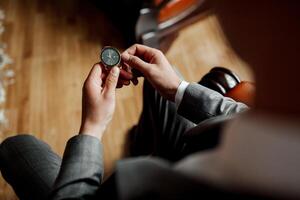 A man is holding a watch in his hand. He is wearing a suit and tie. The watch is black and silver photo