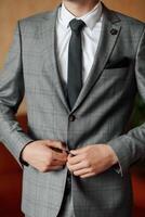 A man in a gray suit and white shirt is adjusting his tie. Concept of formality and professionalism, as the man is dressed in a suit and tie, which is typically worn for business or formal occasions photo
