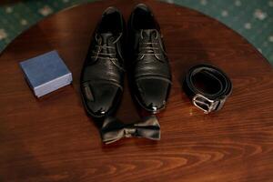A pair of black shoes and a bow tie are displayed on a wooden table photo