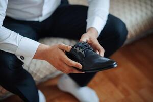 A man is sitting on a couch and holding a black shoe. He is wearing a suit and tie photo