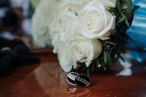 A pair of cufflinks sits on a table next to a bouquet of white roses. The cufflinks are black and have a diamond pattern, while the roses are white and arranged in a vase photo