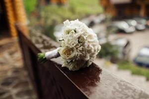 A bouquet of white flowers is sitting on a railing. The flowers are arranged in a way that they look like they are about to be given as a gift. The scene is set in a city photo