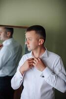 A man is getting dressed in front of a mirror. He is wearing a white shirt and a black suit photo