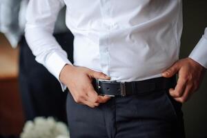 A man in a white shirt and black belt is adjusting his pants. Concept of formality and attention to detail, as the man is making sure his outfit is properly fitted photo