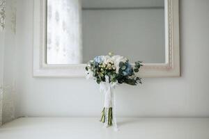 A bouquet of flowers sits on a table in front of a mirror. The flowers are blue and white, and the arrangement is simple and elegant. The mirror reflects the flowers, creating a sense of depth photo