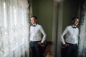 A man in a suit and tie stands in front of a window, smiling. Concept of confidence and happiness, as the man is enjoying his moment. The reflection in the window adds a touch of elegance photo