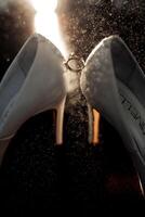 A pair of white shoes with a ring on the left shoe. The shoes are covered in glitter and the ring is shining photo