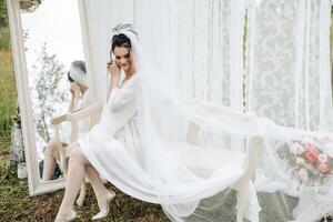 A bride is sitting on a bench with a veil on her head. She is looking at her reflection in a mirror photo