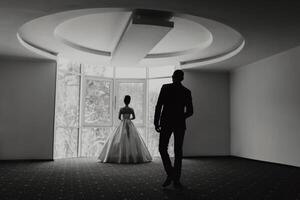 A man and a woman are standing in a room with a window. The man is wearing a suit and the woman is wearing a dress. Scene is romantic and intimate photo