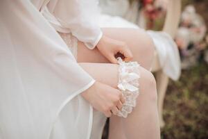 A woman in a white gown is sitting on a chair and adjusting her stockings. The scene is intimate and romantic, with the woman's focus on her appearance photo