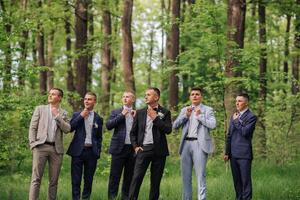 A group of men in suits are standing in a forest. They are all dressed up and looking at something photo